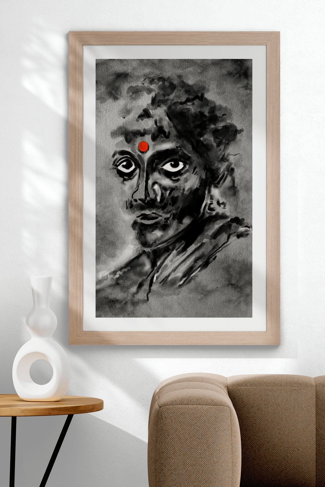 Framed ink portrait of a face with a red bindi, hung on a white wall